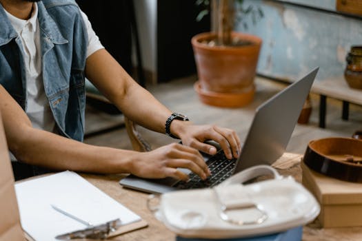 Close-up of hands typing on a laptop indoors with office accessories on a wooden table.