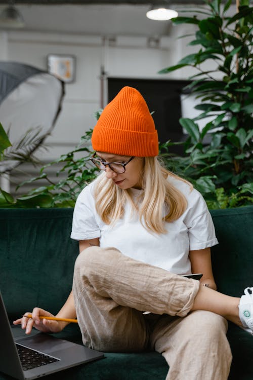 Free Woman in Orange Knit Hat Sitting on Green Sofa Stock Photo