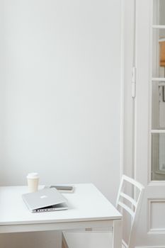 Clean and minimalist workspace featuring a laptop, coffee cup, and phone on a white table.