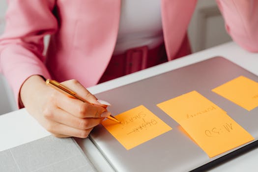 A woman writes on sticky notes placed on a laptop in an office setting.