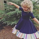 一个快乐的孩子，留着金色卷发，穿着彩色连衣裙在户外跳舞