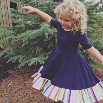 一个快乐的孩子，留着金色卷发，穿着彩色连衣裙在户外跳舞