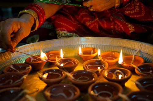 Free A close-up of hands lighting traditional diya oil lamps during a festive celebration indoors. Stock Photo