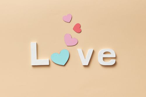 Free Colorful hearts with the word 'Love' on a soft yellow background, perfect for romantic themes. Stock Photo