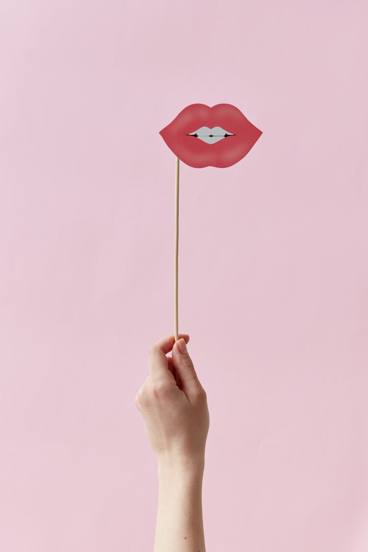
A Person Holding A Mouth With Red Lips Cutout On A Stick