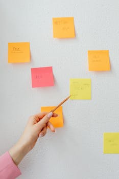 Hand pointing at sticky notes on wall, ideal for creative and planning themes.