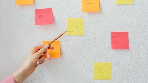 Hand pointing at colorful sticky notes with business concepts on a wall.