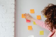 Woman in Pink Long Sleeve Shirt Sticking Post Its on the Wall