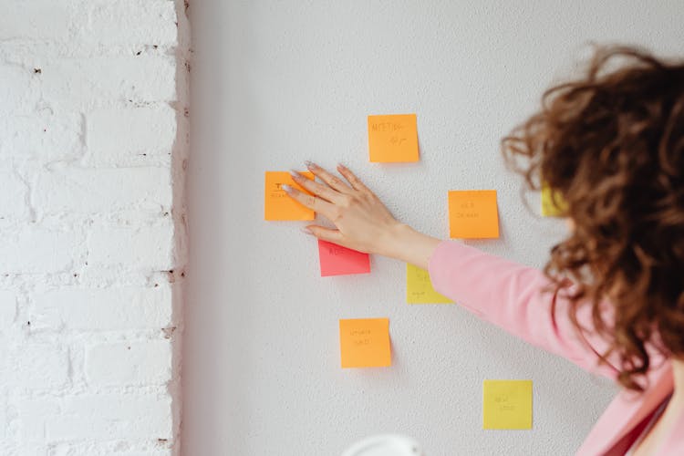 Woman In Pink Long Sleeve Shirt Sticking Post Its On The Wall