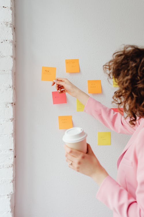 Free 

A Woman in a Pink Blazer Holding a Cup of Coffee while Looking at Sticky Notes on the Wall Stock Photo
