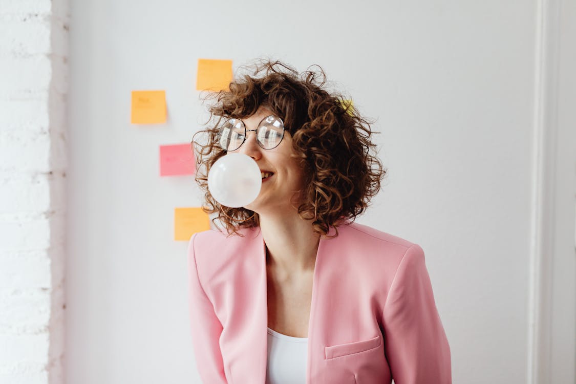 Free Shallow Focus of a Curly-Haired Woman Blowing a Bubble Gum Stock Photo