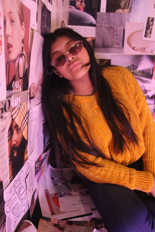 A Woman Wearing a Sweater Leaning on a Wall with Magazine Pages
