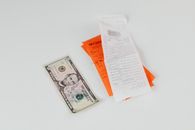 Close-up of a five-dollar bill next to shopping receipts on a white background, ideal for finance and retail themes.