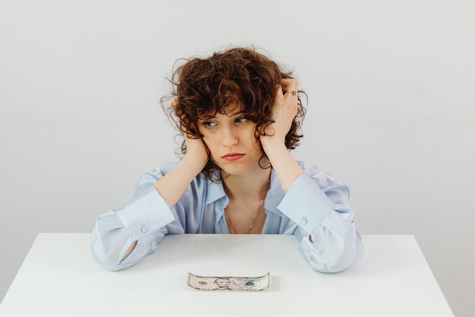 Woman in Blue Long Sleeve Blouse Near the Money on Table