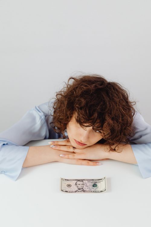 Free Woman with curly hair rests her head on a table gazing at money. Stock Photo
