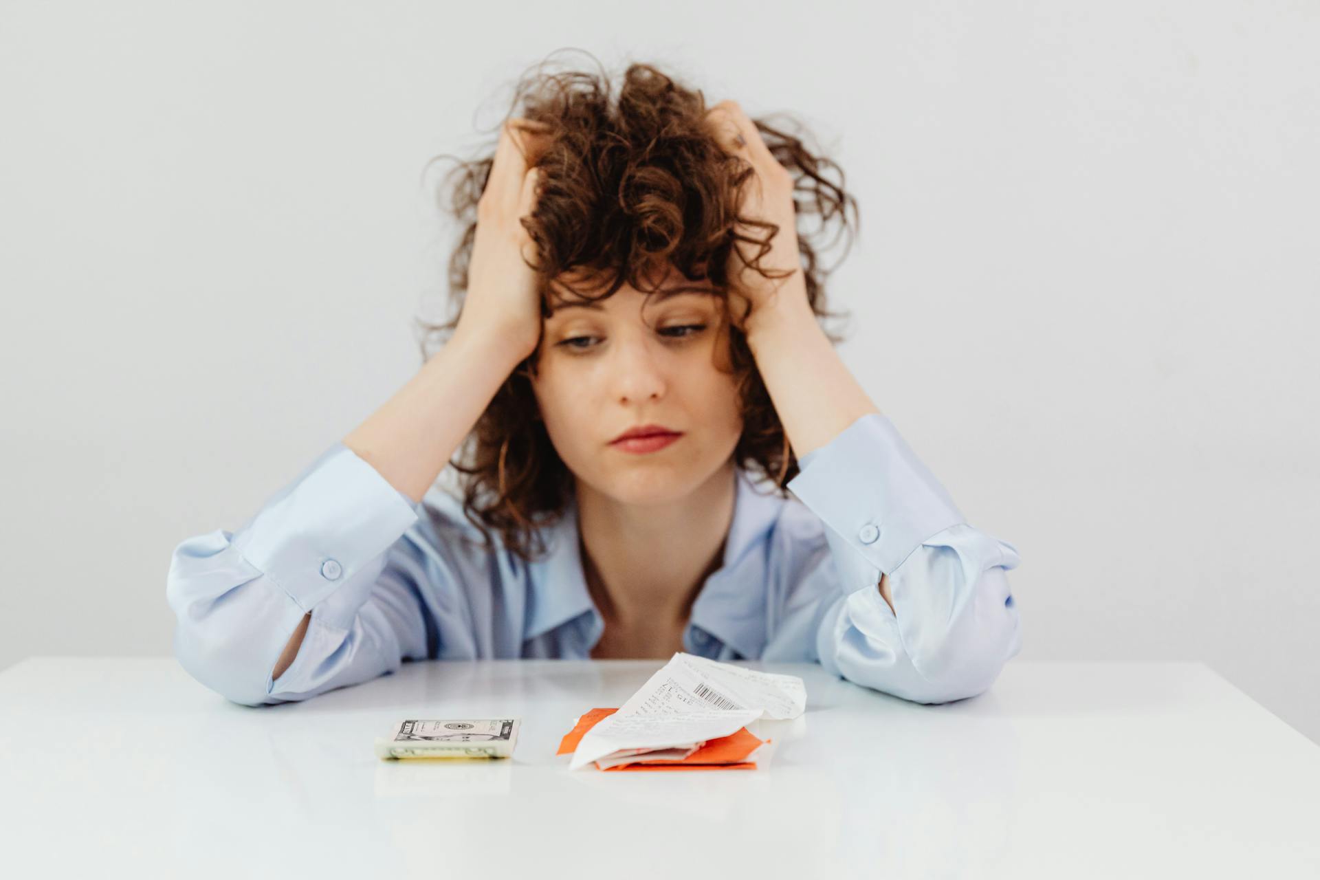 A Tired Woman in Blue Long Sleeves Looking at the Paper Money on the Table