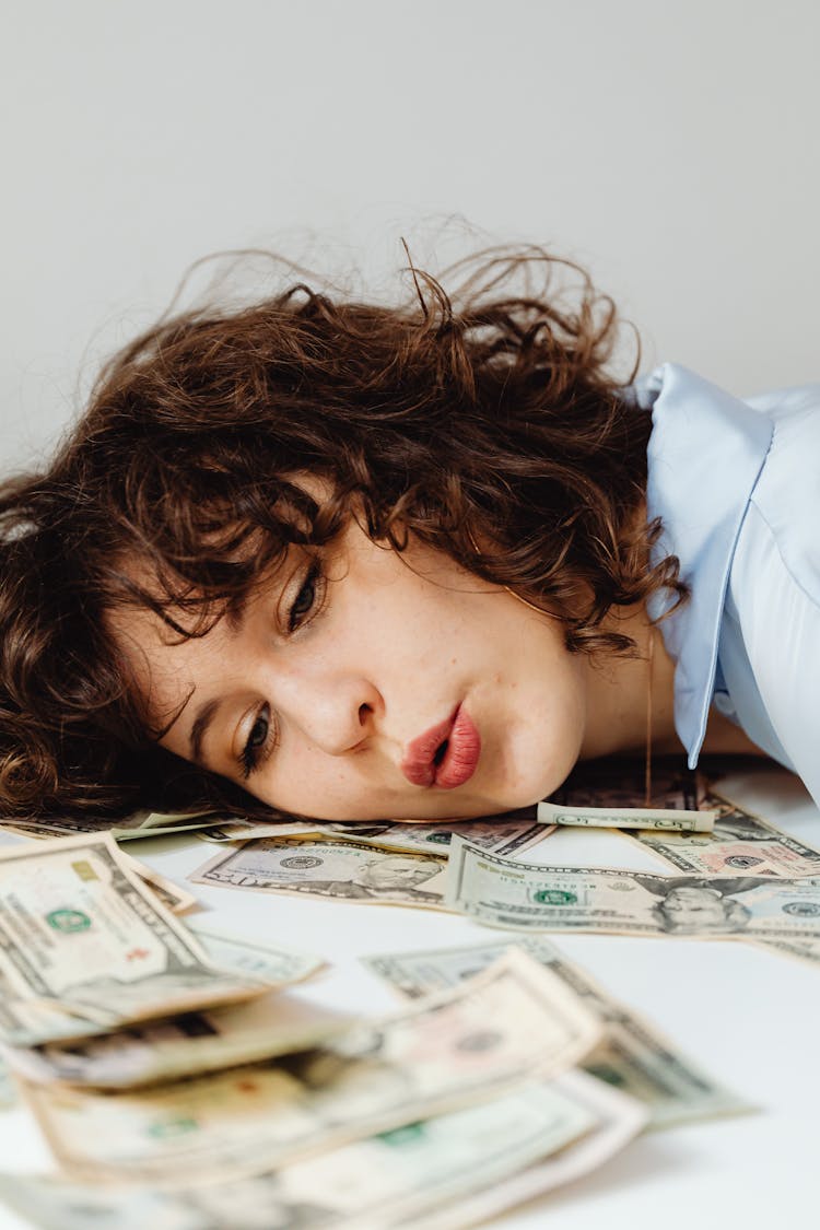 Close-Up Shot Of A Curly-Haired Woman Lying Her Head On Paper Money