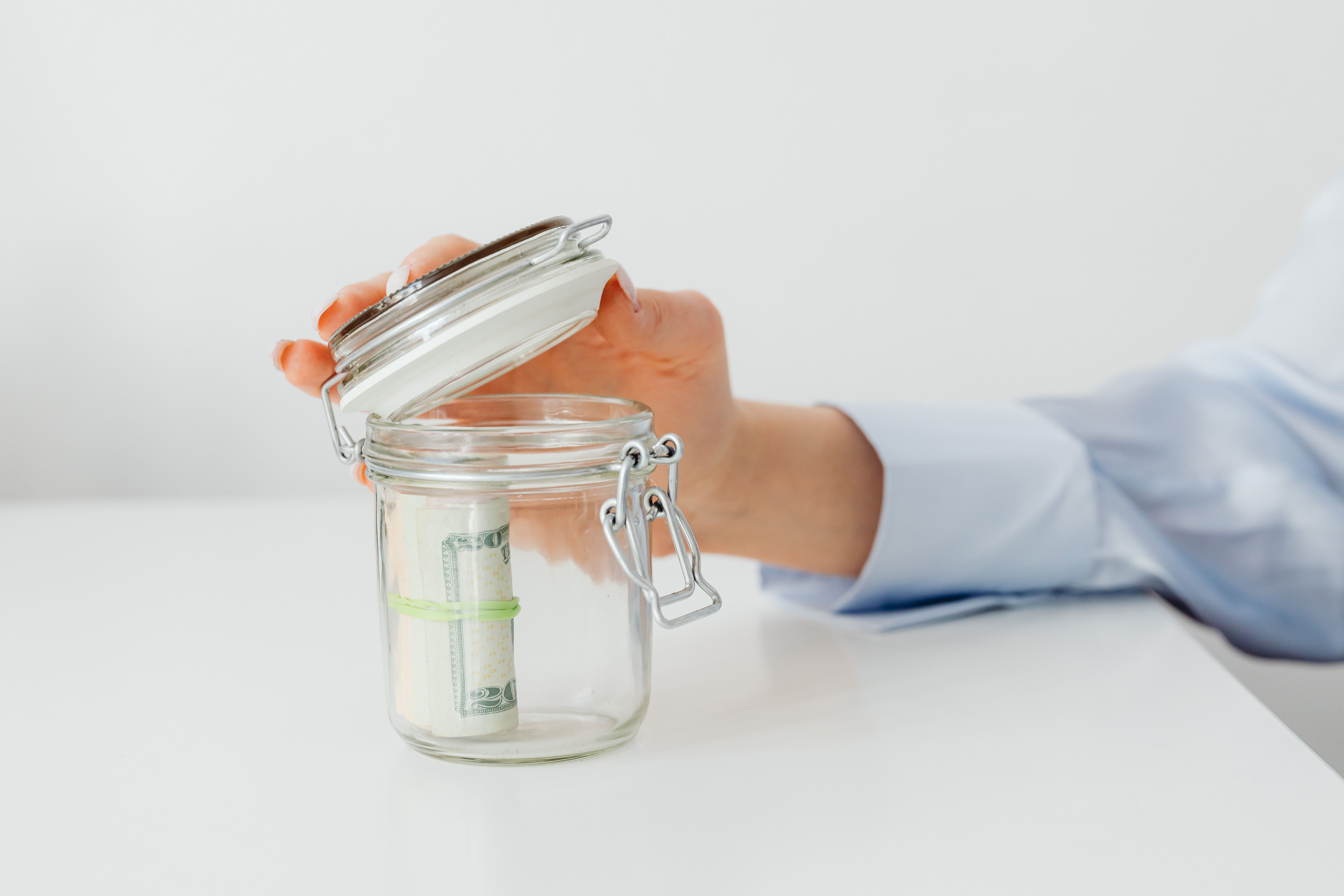 Hand placing cash into a labeled glass savings jar on a table