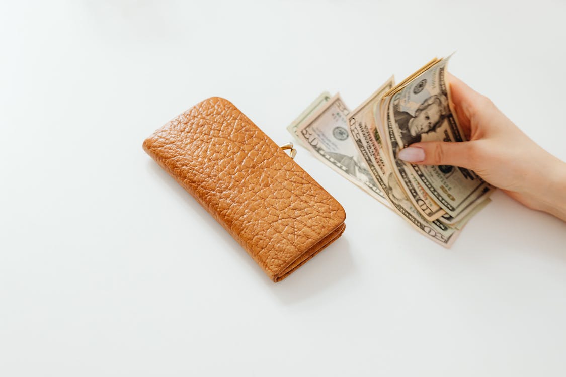 Free Person Holding Money on White Table Beside a Wallet Stock Photo