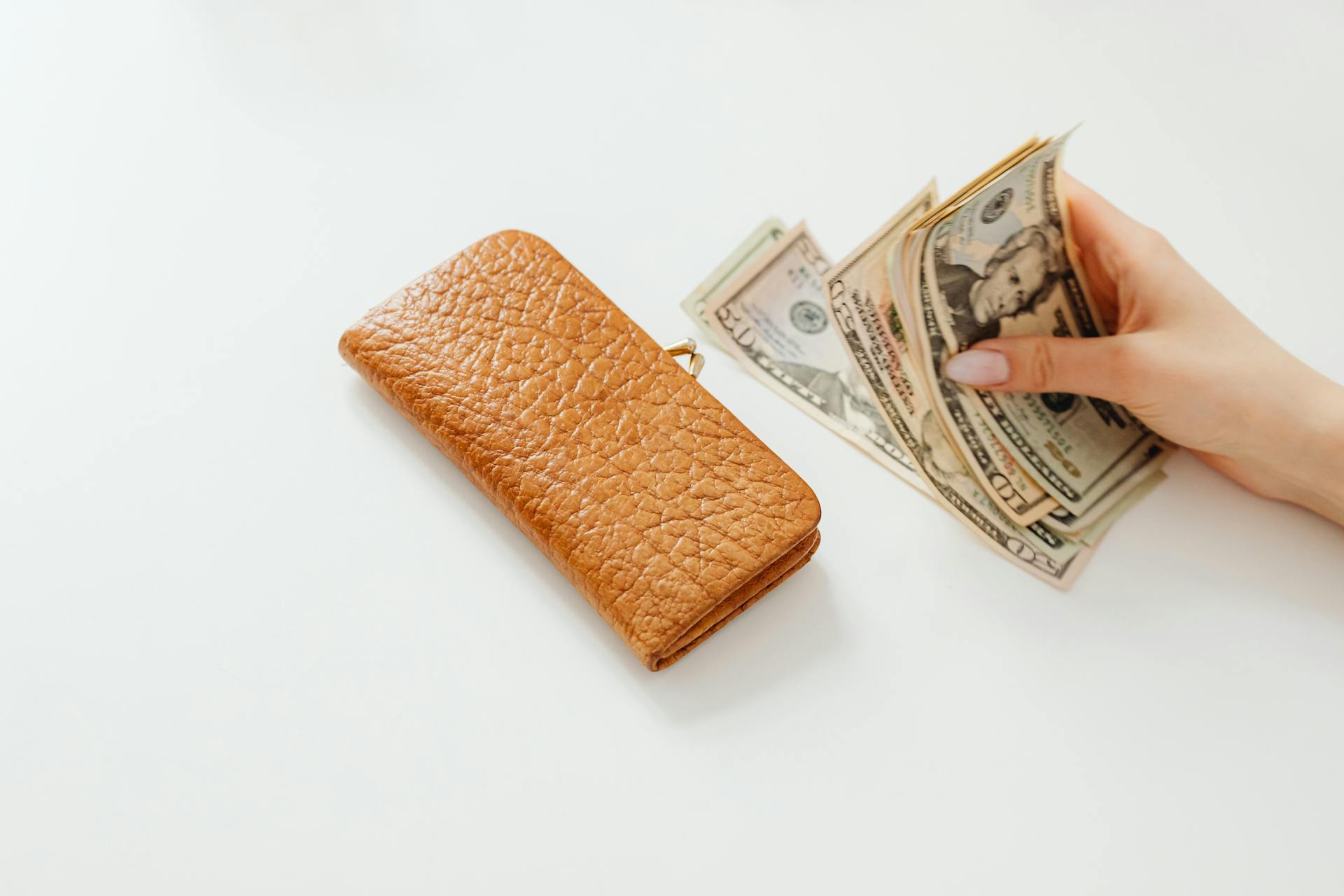 Person Holding Money on White Table Beside a Wallet