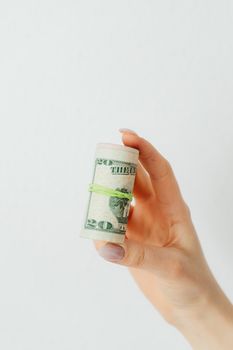 A close-up of a hand with manicured nails holding rolled US dollar bills against a white background.