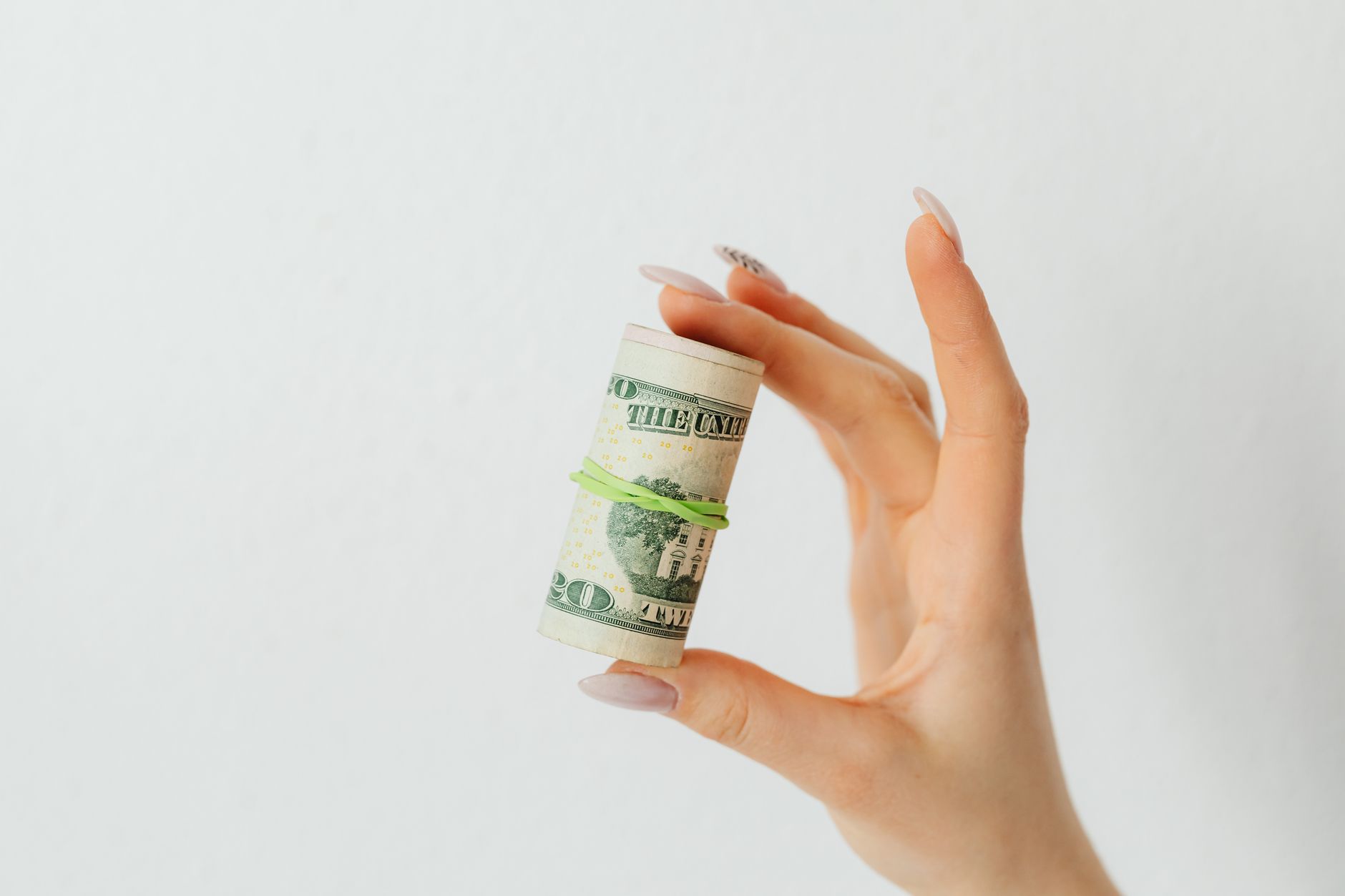 Close-up image of a hand holding a roll of US dollar bills with a rubber band. best ideas to invest money