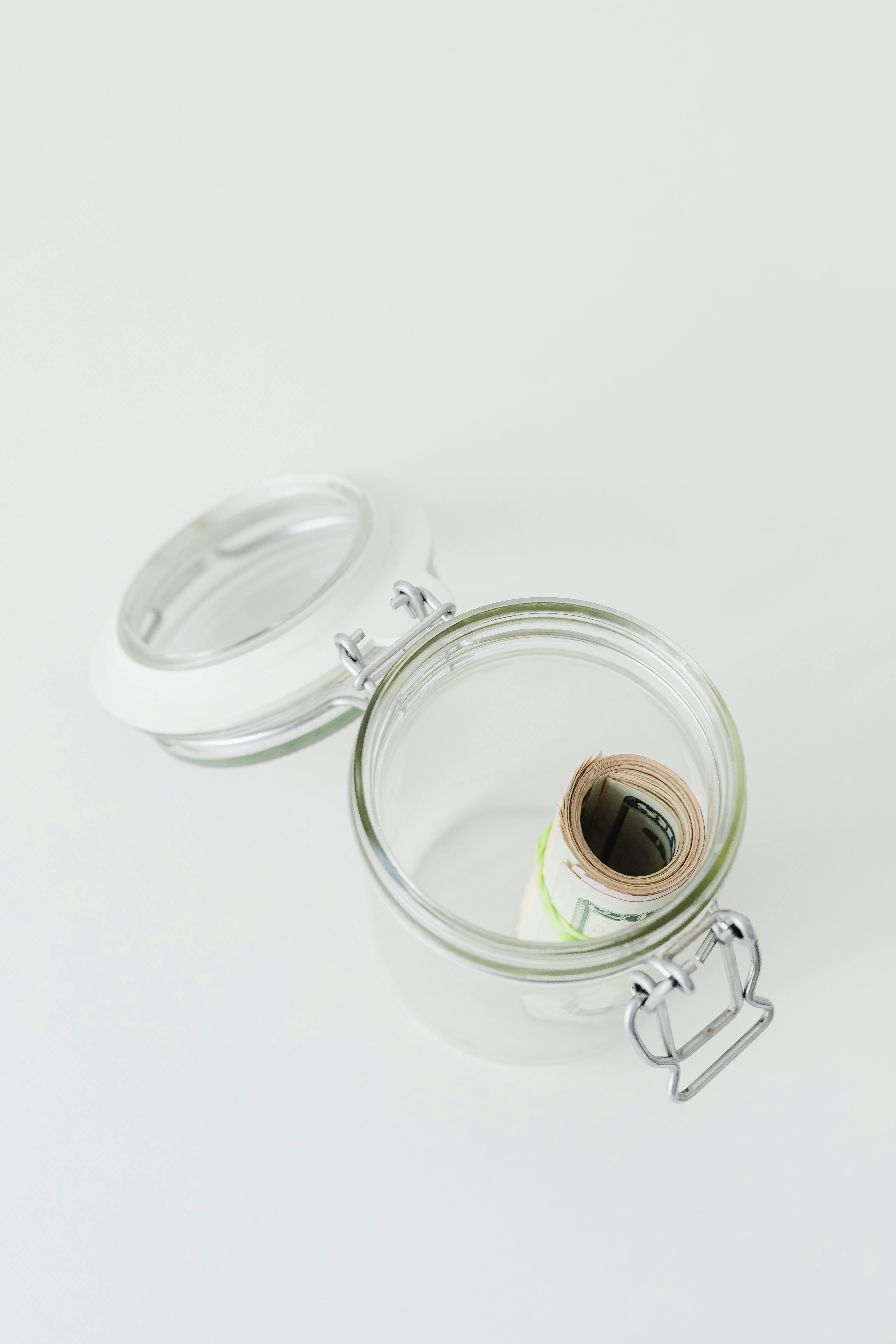 Open glass jar containing rolled paper money, symbolizing savings or finance concept.