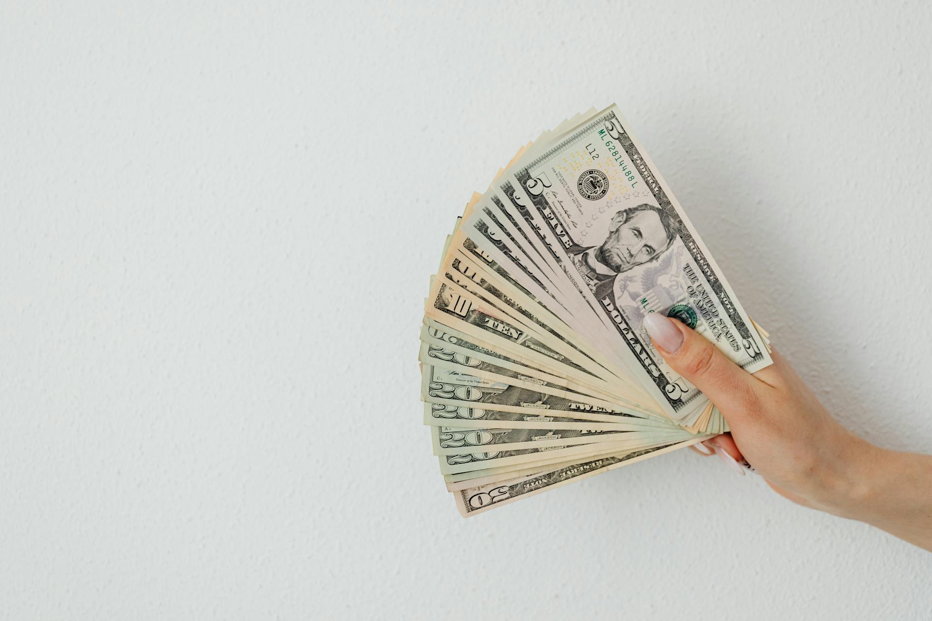 Close-Up Shot of a Person Holding Paper Money on White Surface