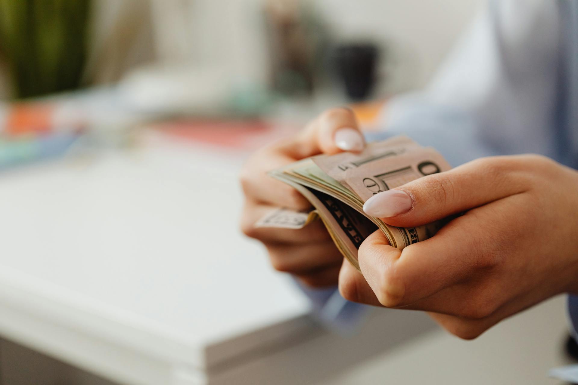 Close-up shot of hands carefully counting US dollar bills indoors at a desk.