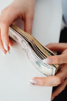 Detailed close-up of hands counting US dollar bills on a white surface.