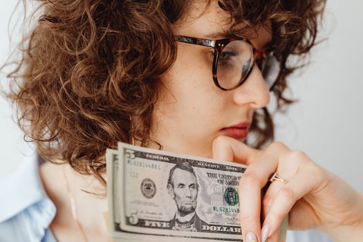Close-up of a woman with glasses holding US dollar bills. Thoughtful expression.