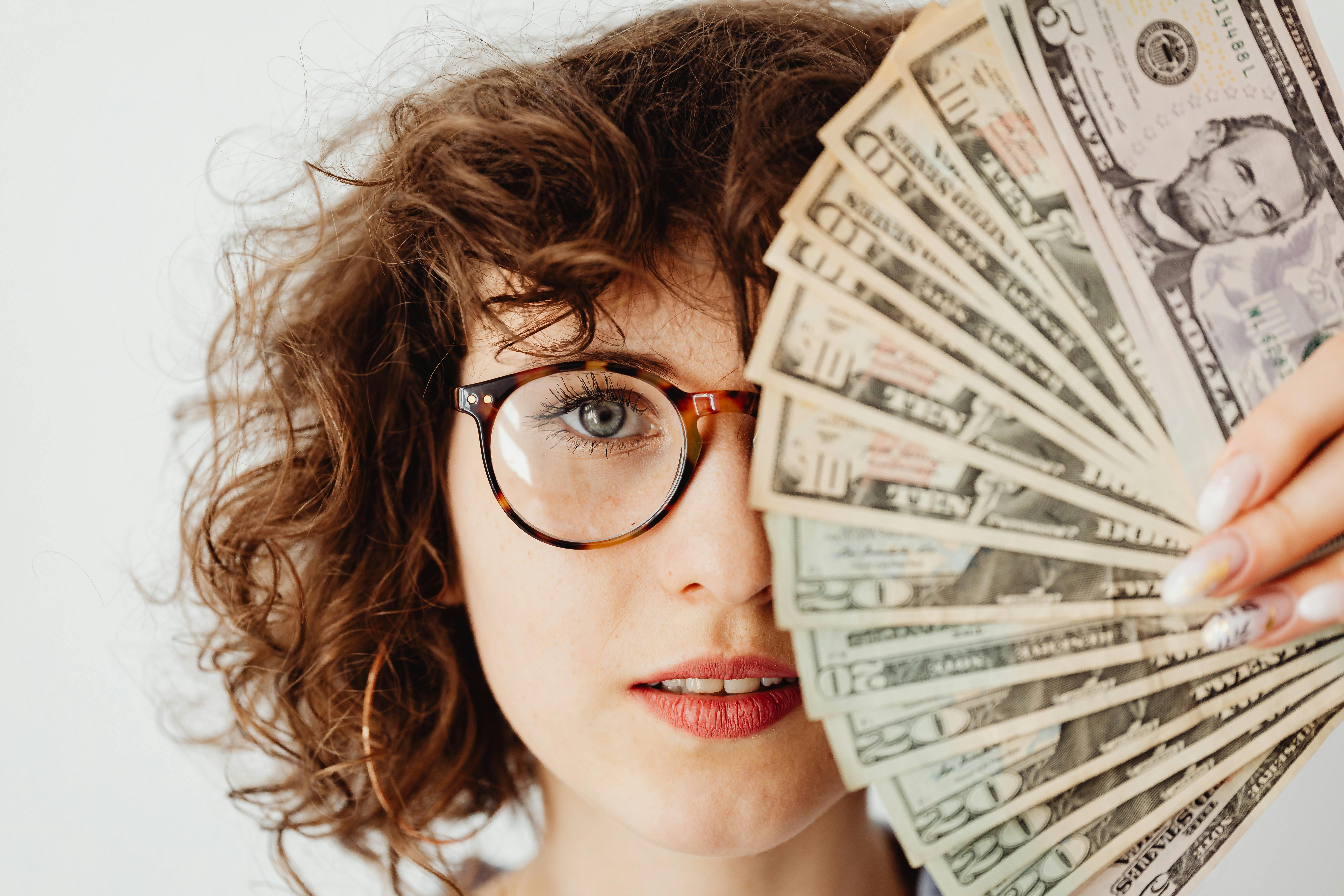woman in eyeglasses covering her face with paper money