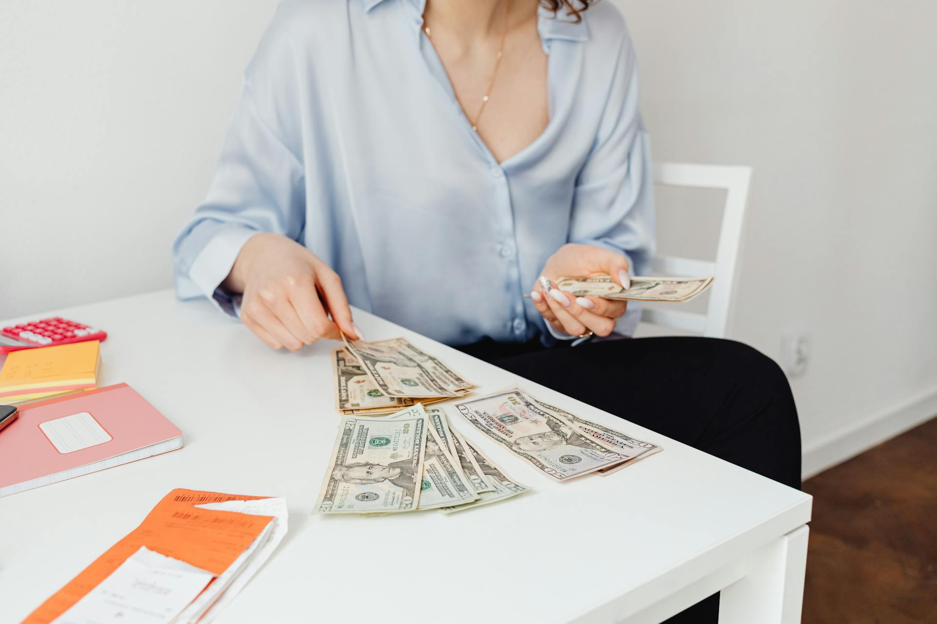 A Person Counting Paper Money on White Table