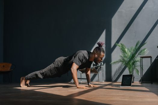 An adult man doing push-ups indoors, guided by a laptop. Fitness and technology merge.