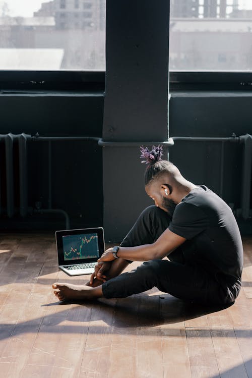 Man Sitting on Wooden Floor while Using His Laptop