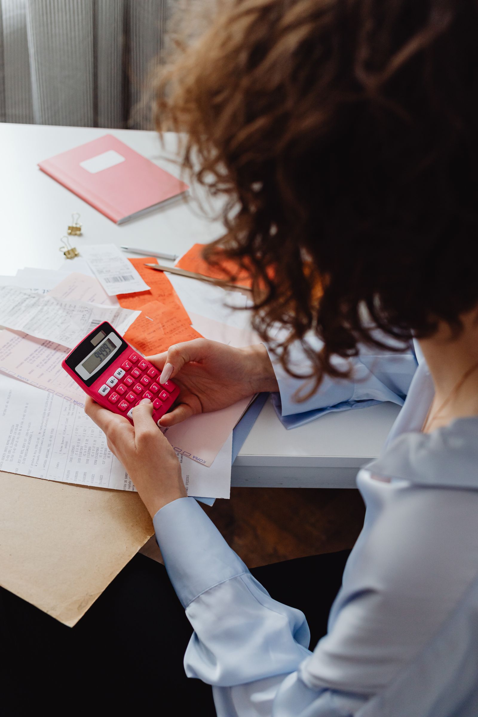 Free Adult woman working with receipts and a bright pink calculator at a desk, focusing on finances. Stock Photo