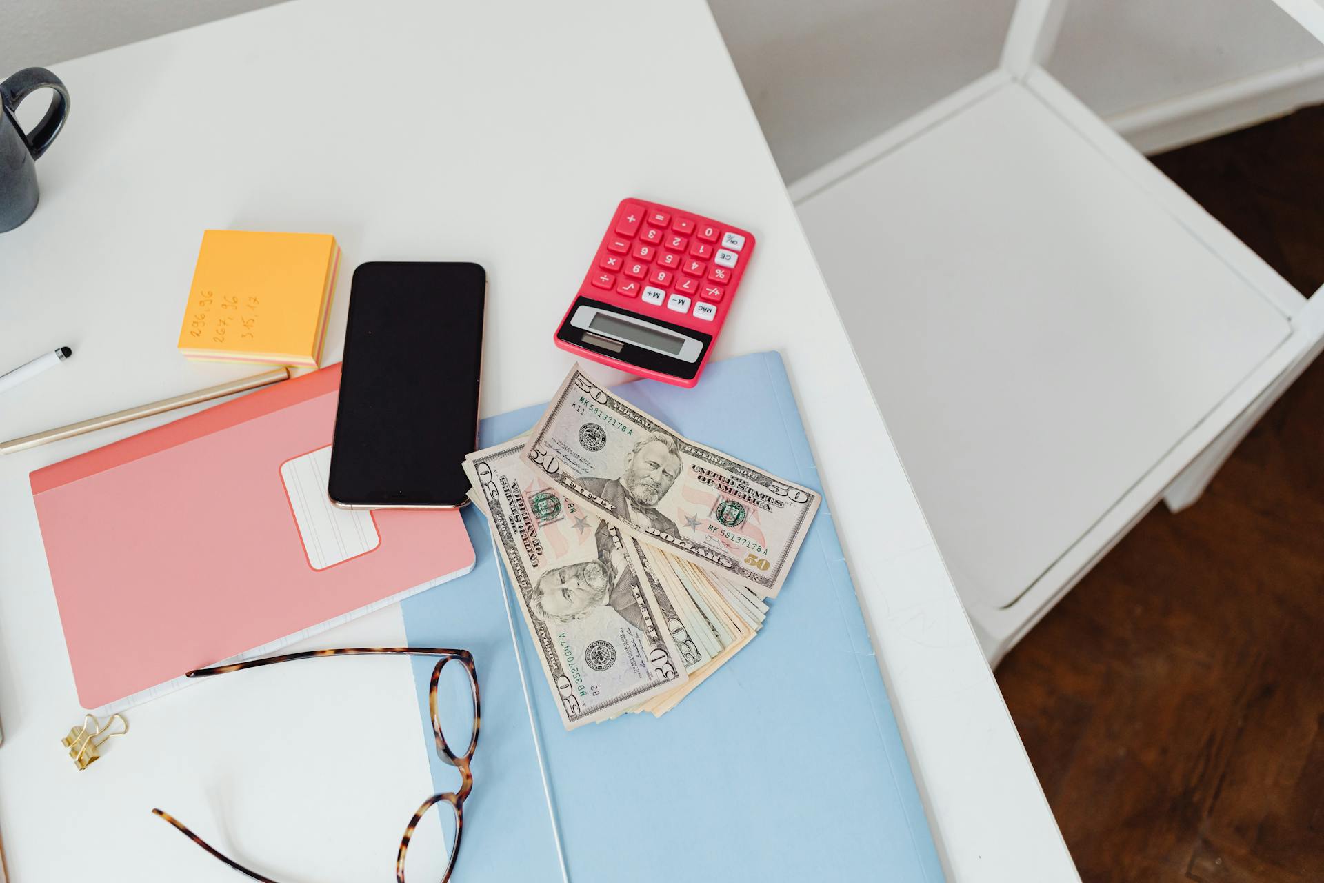 Overhead view of office desk with calculator, money, and glasses, depicting finance and budgeting.