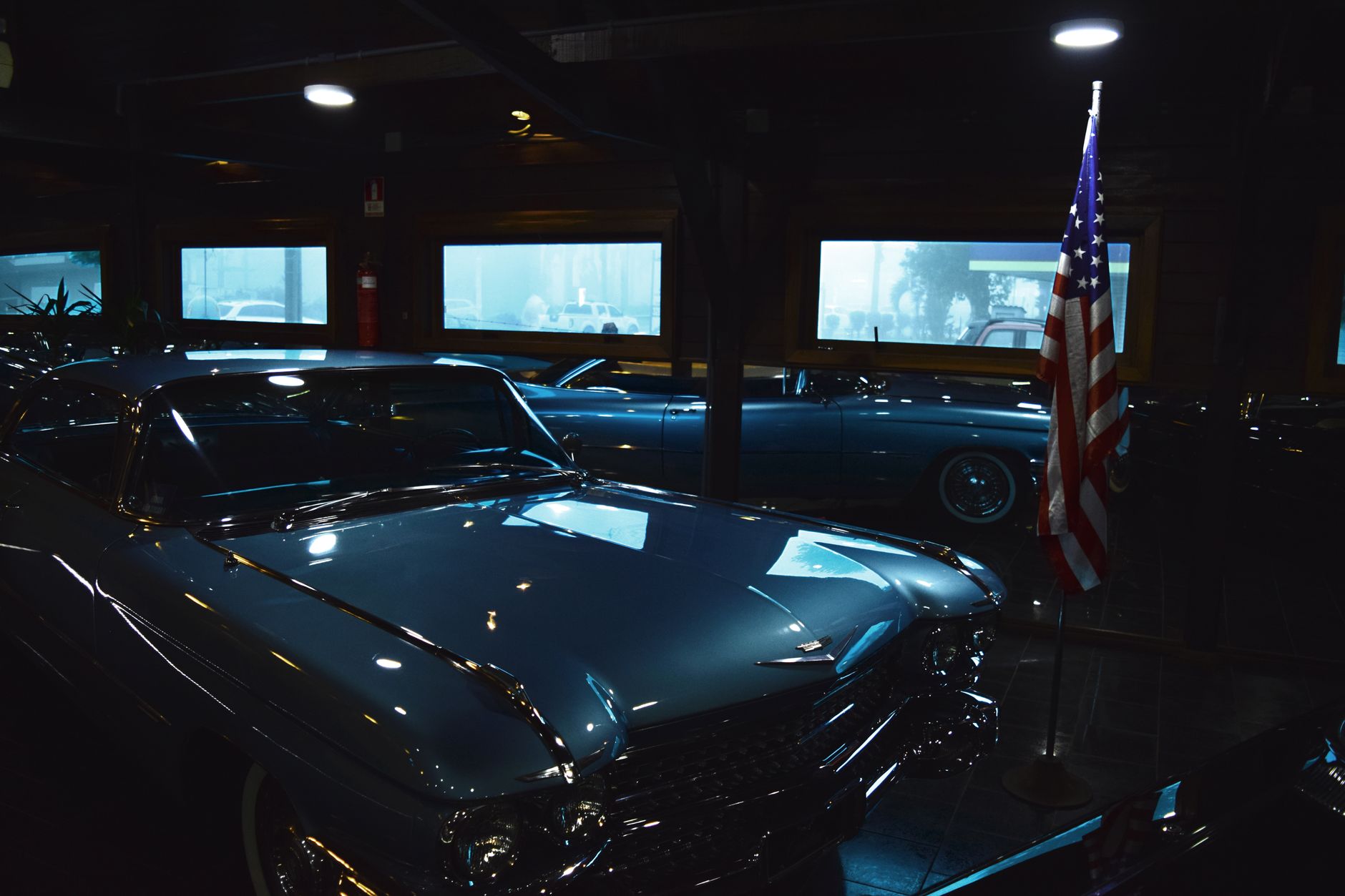 A classic vintage car is showcased indoors alongside an American flag, creating a nostalgic atmosphere.
