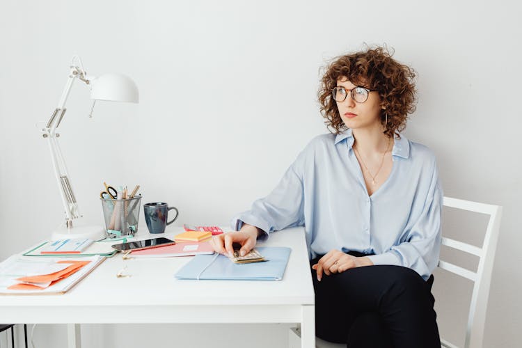 Woman In Blue Long Sleeve Shirt Sitting Sitting At Table Holding Money