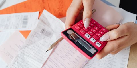 Hands using a pink calculator to manage expenses amidst various receipts and documents.