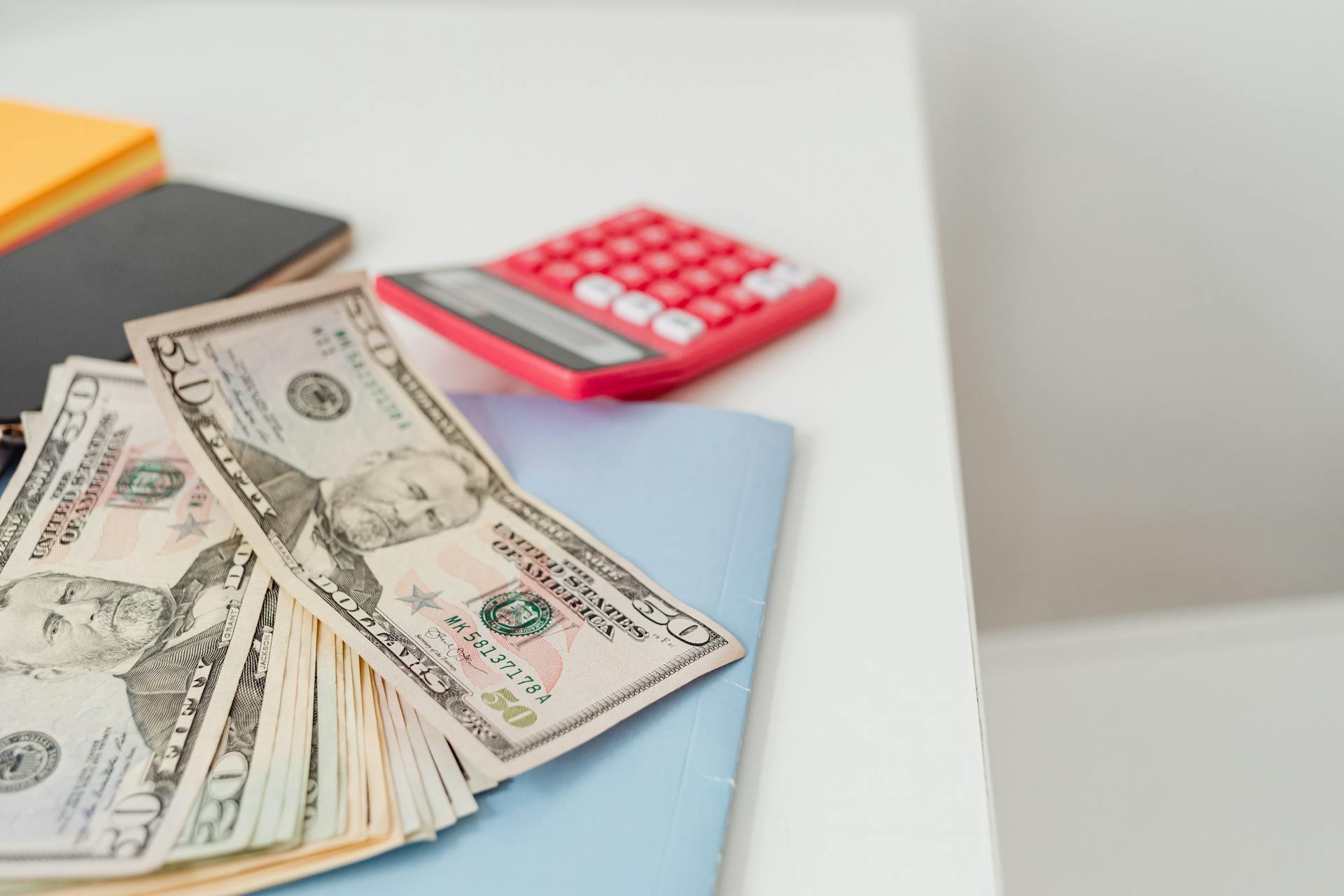 Close-up of notebooks, US dollars, and a calculator on a desk.