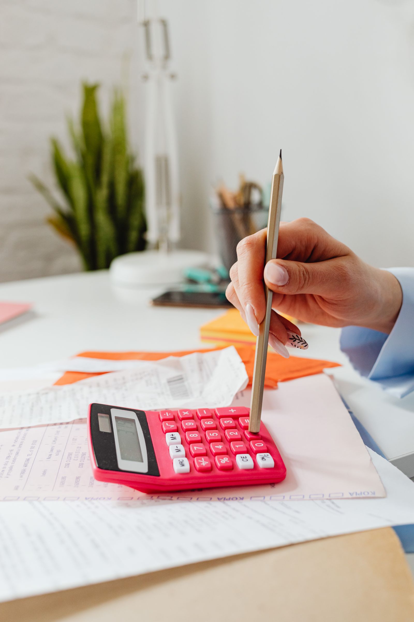 Free Close-up of a hand using a pencil with a red calculator, surrounded by papers indoors. Stock Photo