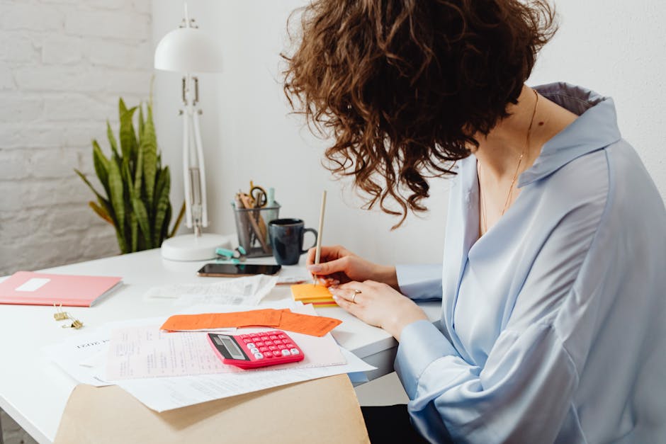 Why Generic Budgeting Fails—Use Free Zero-Based Sheets Woman writing with calculator on desk, managing finances indoors.