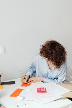 Woman in blue blouse calculating expenses at a modern workspace. Bright and focused atmosphere.