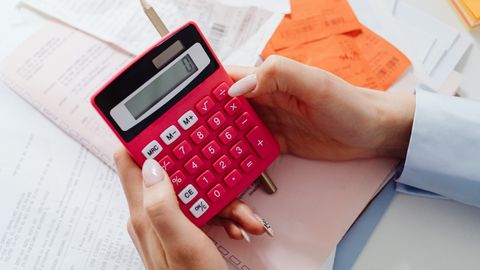 Close-up of hands holding a red calculator, managing finances with documents and receipts.