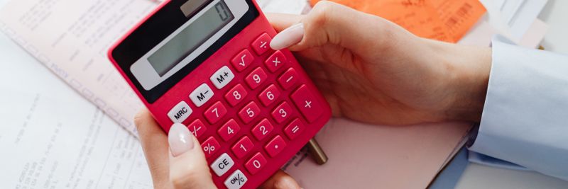 Close-up of hands holding a red calculator, managing finances with documents and receipts.