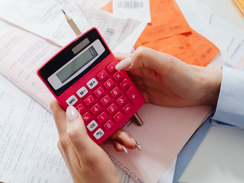 Close-up of hands holding a red calculator, managing finances with documents and receipts.