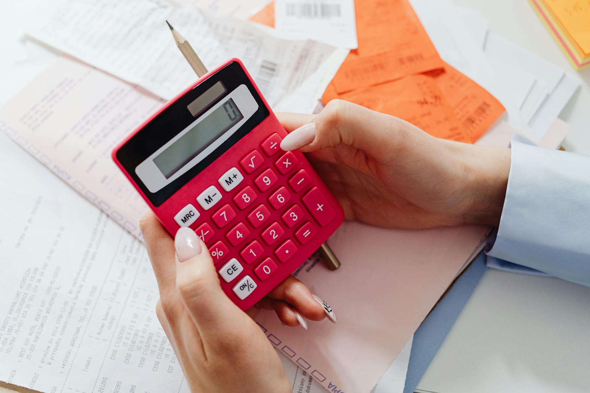 Close-up of hands holding a red calculator, managing finances with documents and receipts.