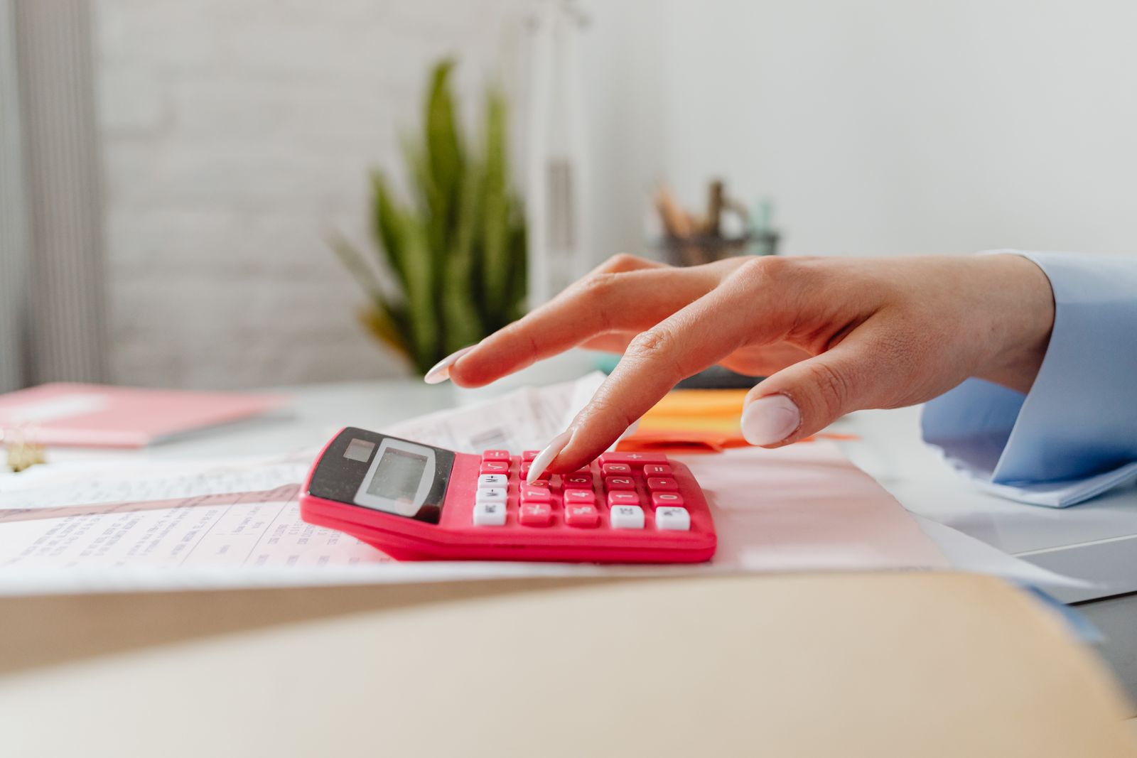 Free A close-up image of a person's hand using a red calculator on a desk with paperwork. Stock Photo