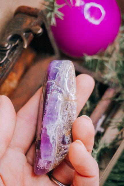 A hand holds a polished amethyst crystal amidst festive decorations and greenery indoors.